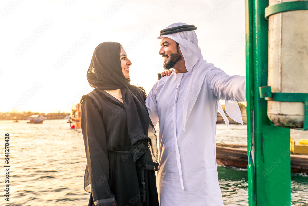 Middle eastern couple of lovers wearing traditional emirati clothing dating outdoors in Dubai - Modern arabian couple meeting and having fun in the city