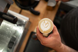 Professional barista holding paper cup with latte foam over coffee, espresso and creating a perfect cappuccino