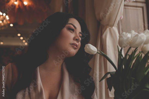 Beautiful woman drressed biege elegant suit sit in cafe and drink the cup of coffee. The plus size woman holding a bouquet of whine flowers. Happy overweight model