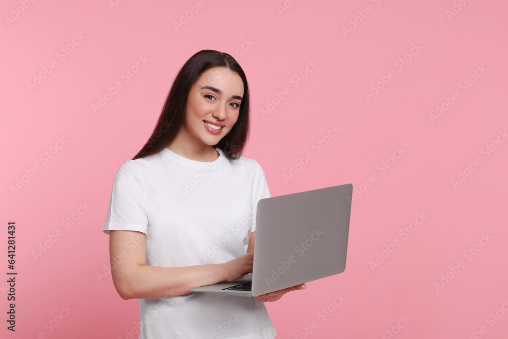 Smiling young woman working with laptop on pink background, space for text Smiling young woman working with laptop on pink background, space for text