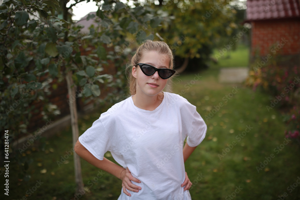 beautiful stylish girl in black sunglasses and a white t-shirt on a green background. the girl is standing in the garden with collected hair