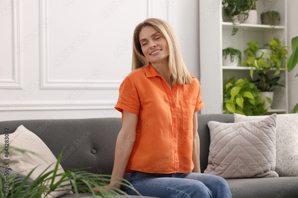 Woman sitting on sofa in room with beautiful houseplants Woman sitting on sofa in room with beautiful houseplants