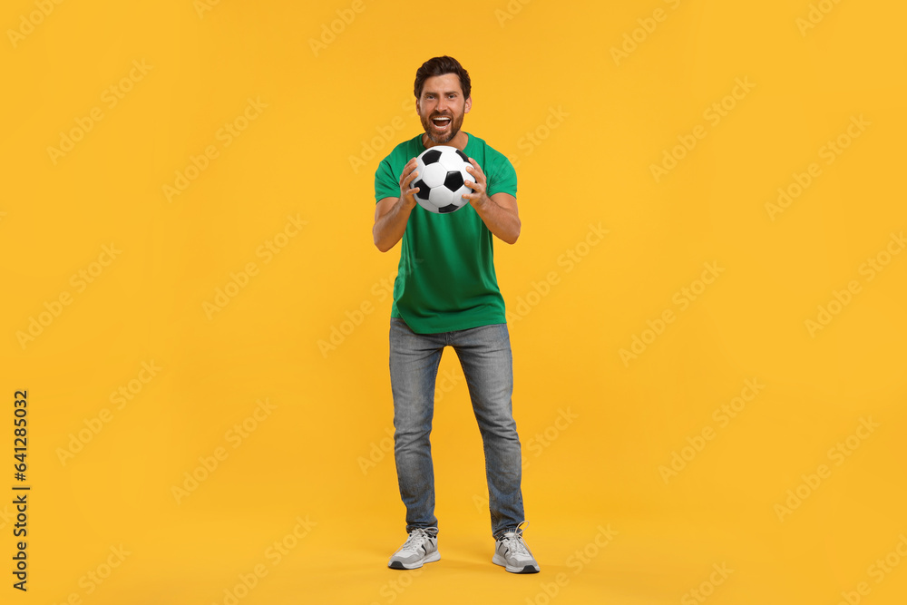 Emotional sports fan with soccer ball on orange background Emotional sports fan with soccer ball on orange background