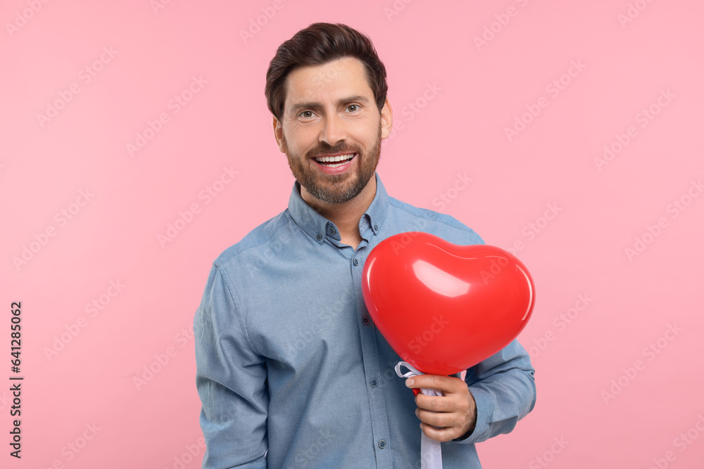 Happy man holding red heart shaped balloon on pink background Happy man holding red heart shaped balloon on pink background
