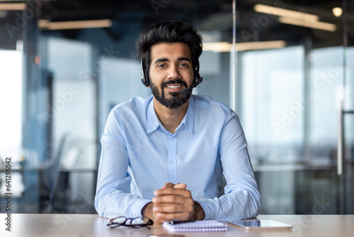 Portrait of a young Indian male teacher in a headset sitting in the office in front of the camera and teaching talking online
