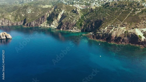 The drone flies over the crystal clear sea with turquoise water along the rocky coast of Sardinia island in Italy