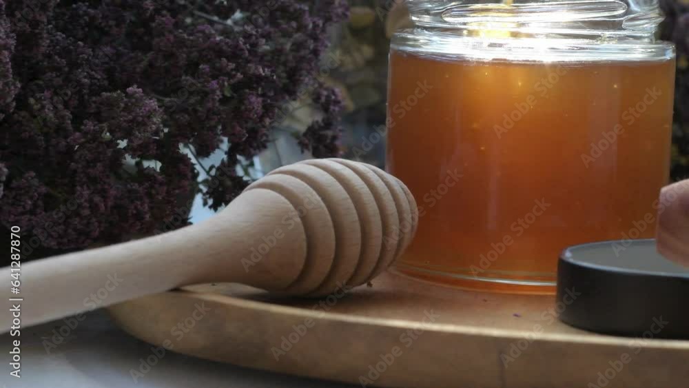 fresh natural linden honey in glass jar with wooden honey spoons around herb flowers. close up fresh natural linden honey in glass jar with wooden honey spoons around herb flowers. close up