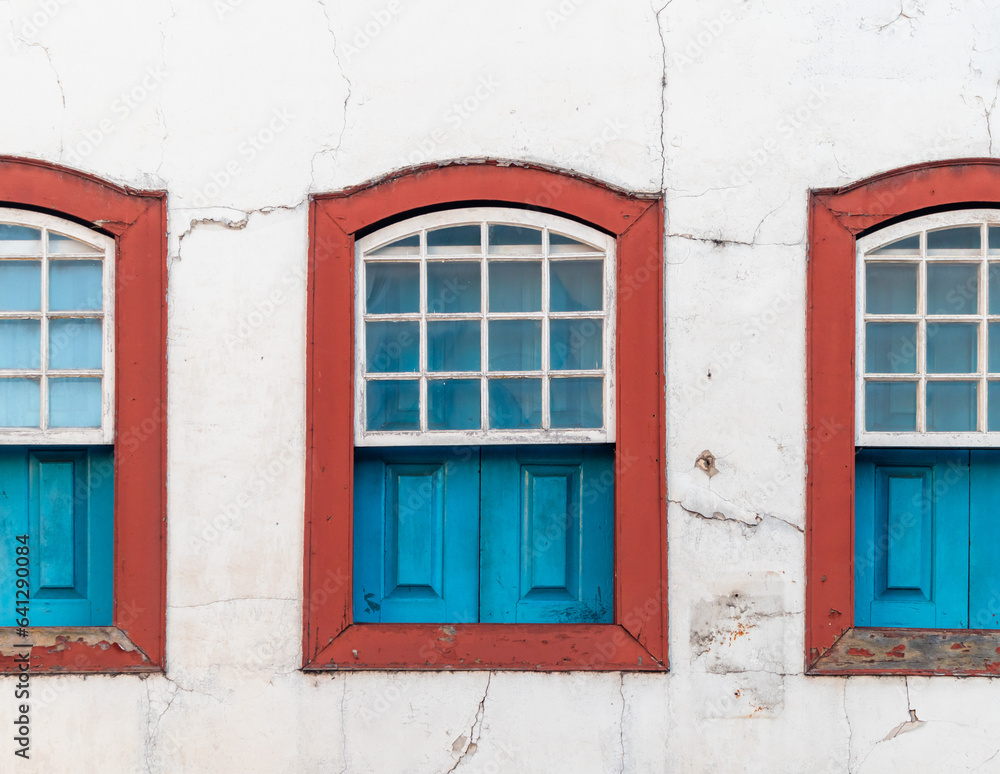 Decorative windows, blue and red, colonial, vintage, on a white wall with cracks. Brazilian colonial old houses
