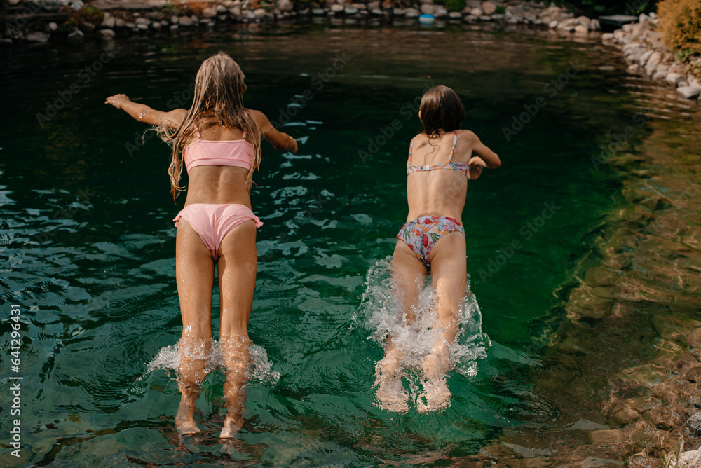 Fototapeta premium Two little girls jump in swimsuits into a lake with cold water on a hot summer day