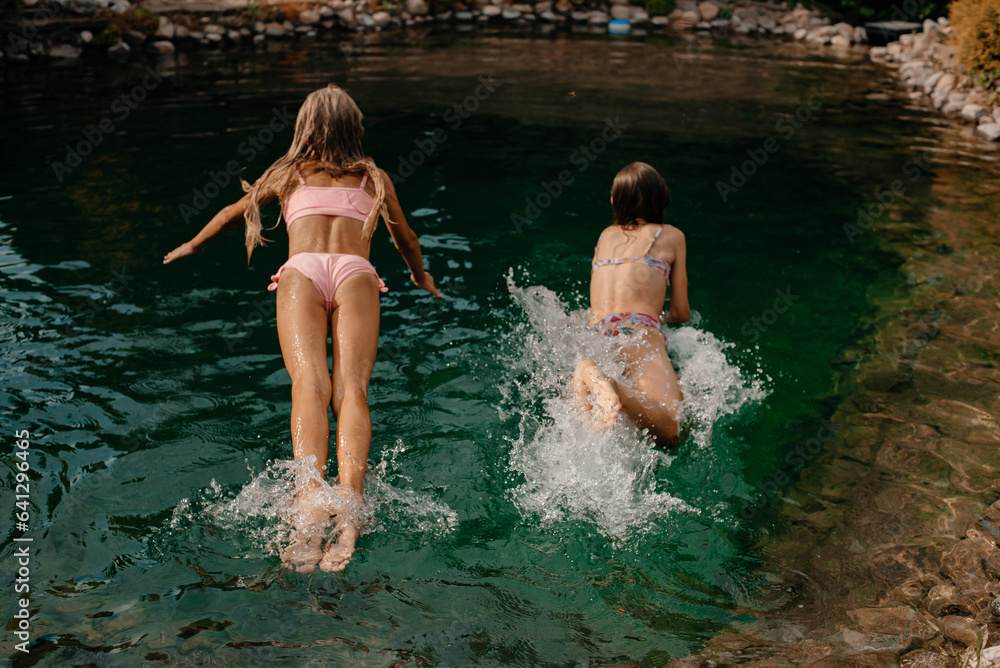 Fototapeta premium Two little girls jump in swimsuits into a lake with cold water on a hot summer day
