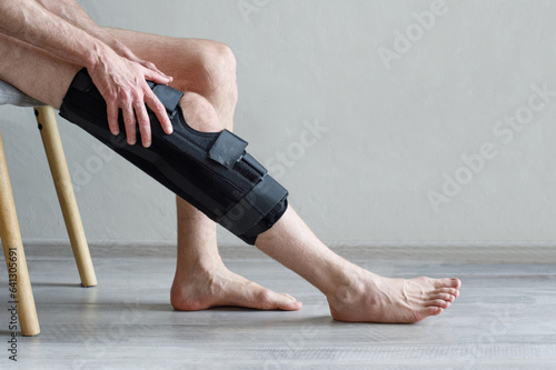 Knee Brace on male leg on grey background. Orthopedic Anatomic Orthosis. Braces for knee fixation, injuries and pain. Foot orthosis tutor