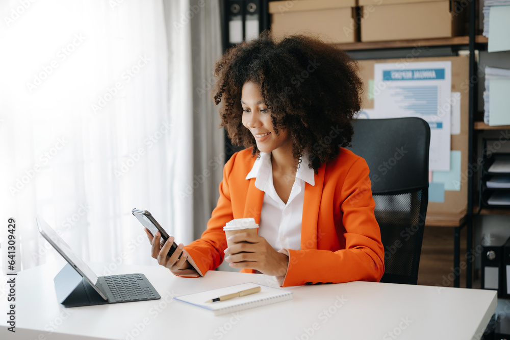 Young African woman typing on tablet and laptop while sitting at the working wooden table modern office Young African woman typing on tablet and laptop while sitting at the working wooden table modern office