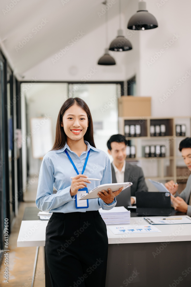 Young attractive Asian female office worker business suits smiling at camera in office . Young attractive Asian female office worker business suits smiling at camera in office .