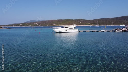 Young man walking in shallow water and a Yacht boat moored to wooden jetty dock in Blue lagoon, Veliki Budikovac island. Aerial photo