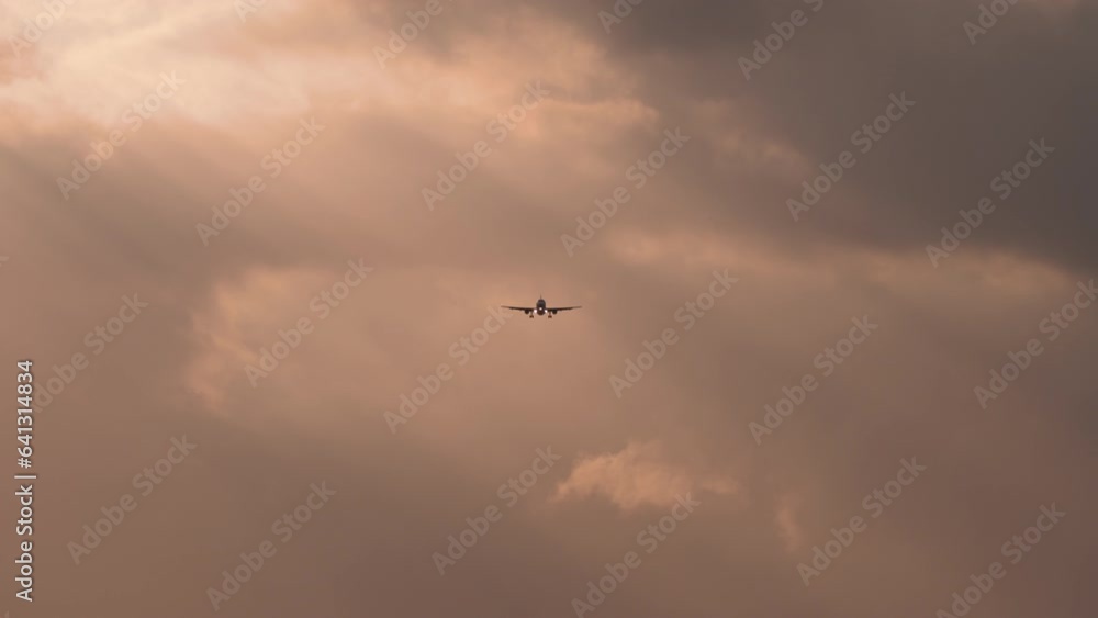 Dark silhouette of an airplane landing in the sun. Cloudy sunset. Jet plane approaching, long shot Dark silhouette of an airplane landing in the sun. Cloudy sunset. Jet plane approaching, long shot