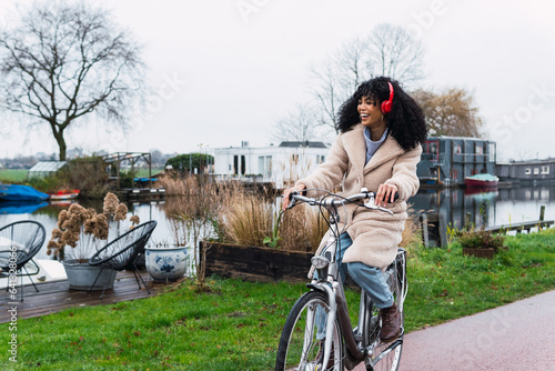 Canvas Print Young happy woman with headphones rides a bicycle in city street