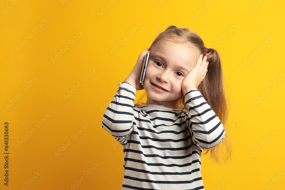 Funny little girl talking on mobile phone on yellow background. Funny little girl talking on mobile phone on yellow background.