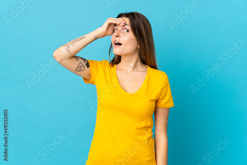 Young slovak woman isolated on blue background doing surprise gesture while looking to the side