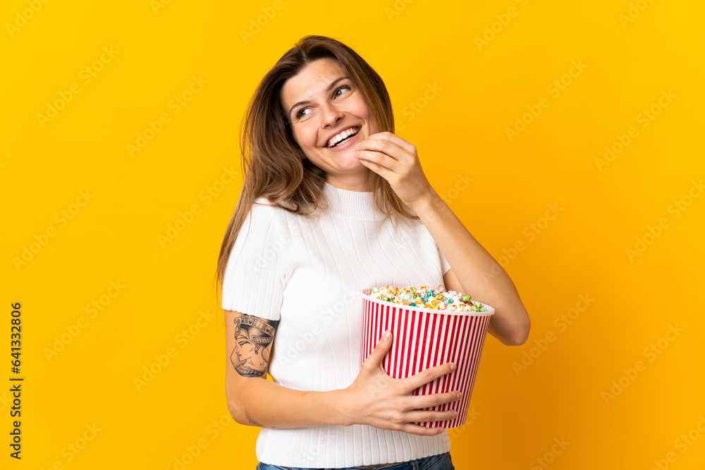 Young slovak woman isolated on yellow background holding a big bucket of popcorns Young slovak woman isolated on yellow background holding a big bucket of popcorns