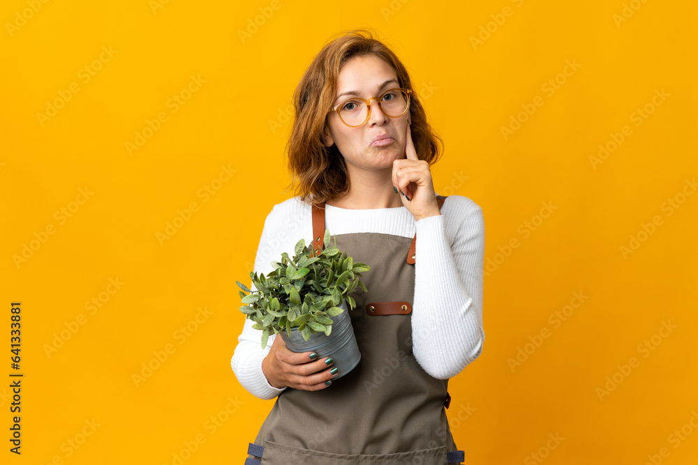 Young Georgian woman holding a plant isolated on yellow background thinking an idea Young Georgian woman holding a plant isolated on yellow background thinking an idea