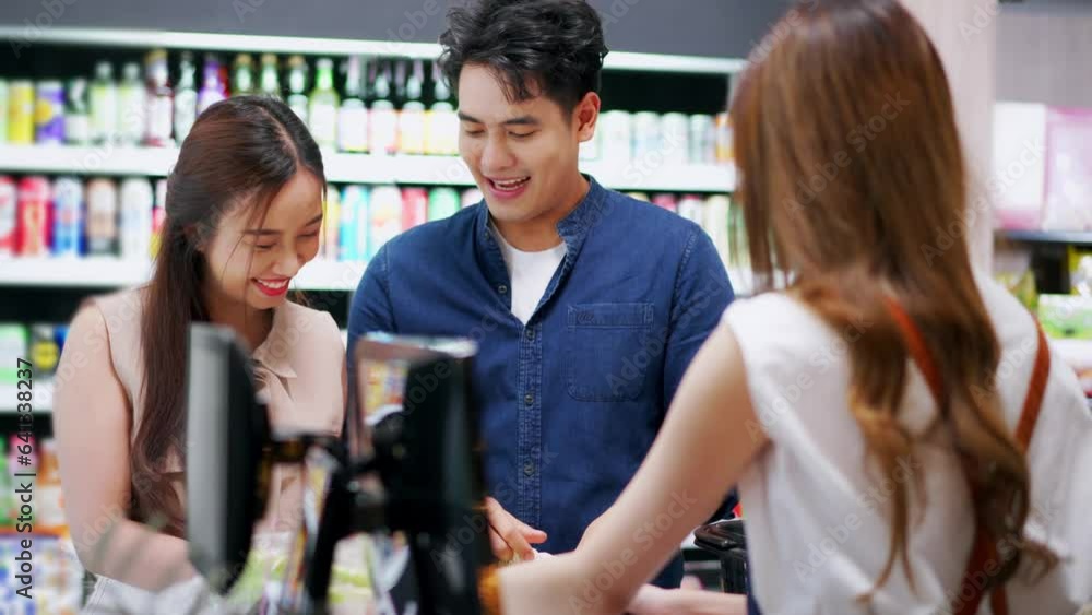 Asian happy couple talking to cahier while putting groceries into the shopping bag on checkout counter in the supermarket Asian happy couple talking to cahier while putting groceries into the shopping bag on checkout counter in the supermarket