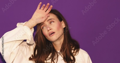 Brunette woman faint, dramatically put hand on head and fall. Girl wear white jeans jacket isolated on purple background.