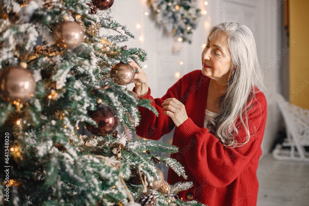 Senior woman standing and decorating christmas tree Senior woman standing and decorating christmas tree