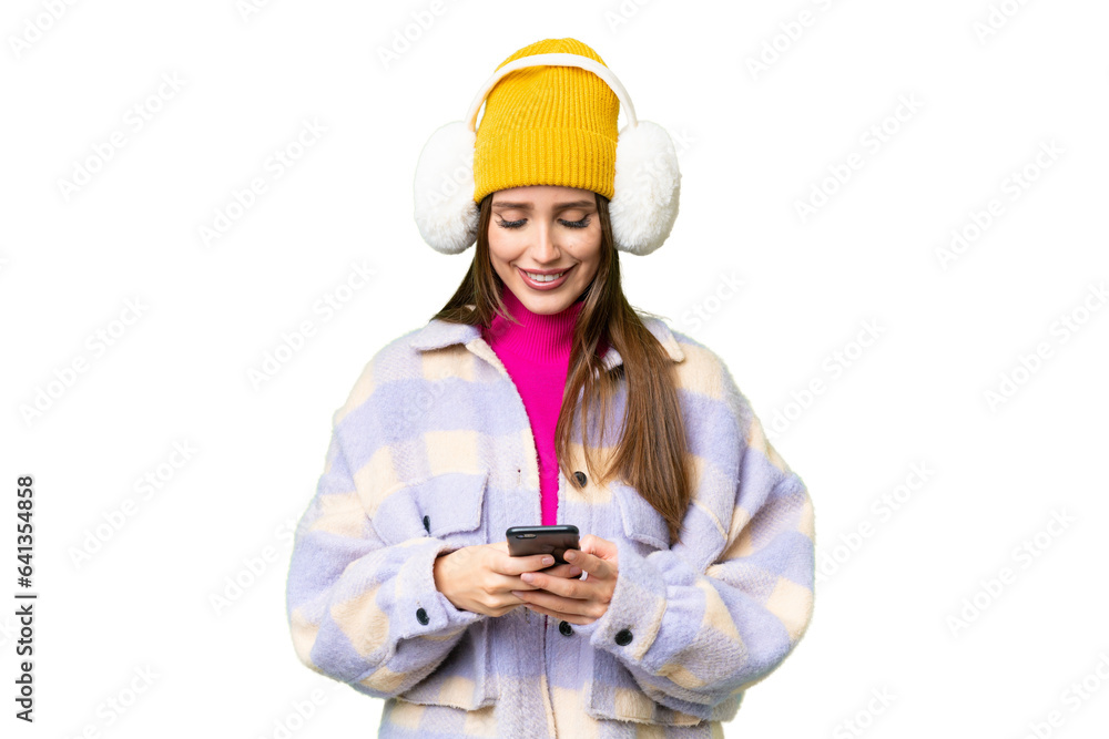 Young woman wearing winter muffs over isolated chroma key background sending a message with the mobile