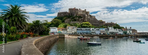 Obraz  z motywem Panoramic image of Mont Orgueil Castle in Gorey on the island of Jersey in the Channel Islands. Fishing boats and colourful buildings with sunshine and blue sky