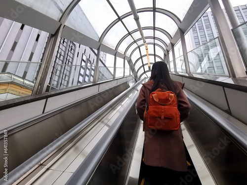 A young female tourist is standing on an escalator to get out of the subway station onto the street.