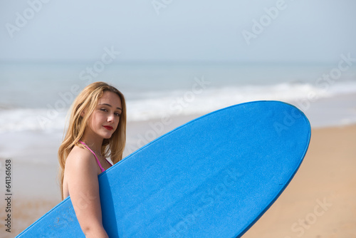 Young and beautiful blonde surfer woman in pink bikini and blue surfboard. The girl enjoys her holidays on the beach to practice her favourite sport. Travel and holiday concept © @skuder_photographer