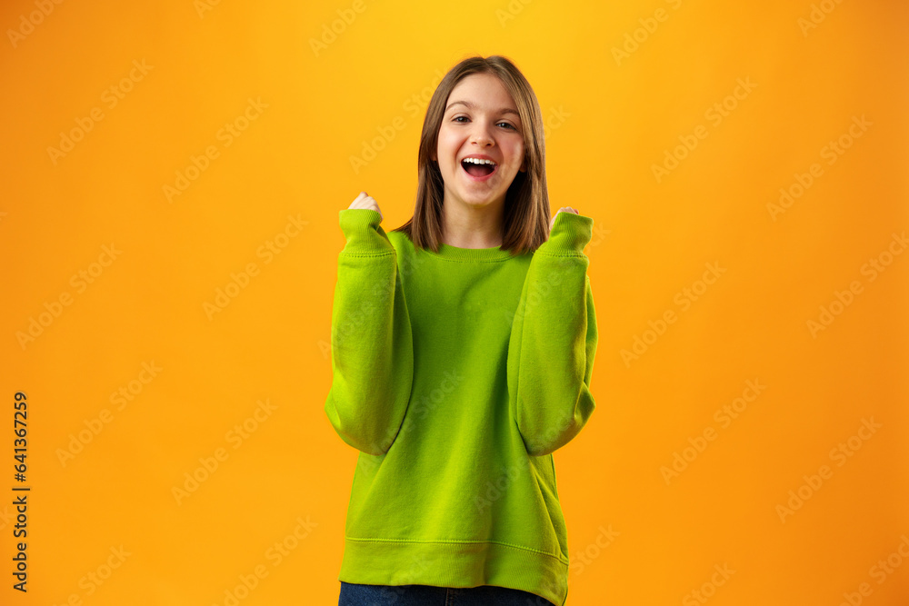 Portrait of a joyful happy teenage girl celebrating success on yellow background Portrait of a joyful happy teenage girl celebrating success on yellow background