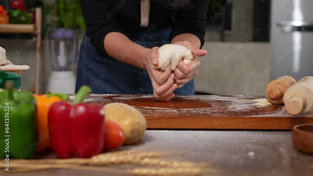 A joyful woman wearing apron standing in kitchen and kneading pizza dough on table. Making dough by hand in a bakery. Preparing dough for pizza at home, preparation of pizza bread or cake process. A joyful woman wearing apron standing in kitchen and kneading pizza dough on table. Making dough by hand in a bakery. Preparing dough for pizza at home, preparation of pizza bread or cake process.