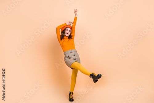 Full length photo of carefree cheerful overjoyed adorable lady wear orange clothes have fun empty space isolated on beige color background