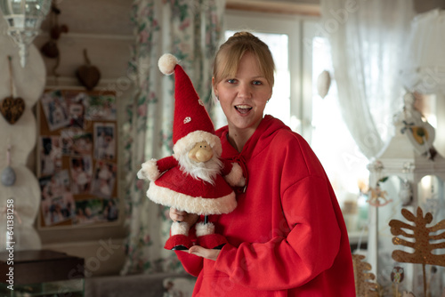 A young girl in a red hoodie holds a toy Santa Claus in her handsA young girl in a red hoodie holds a toy Santa Claus in her hands photo