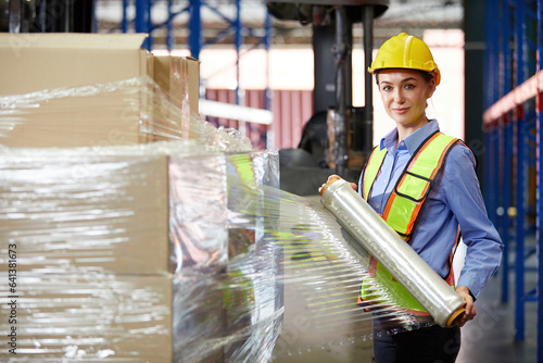 factory worker or warehouser wrapping stretch film parcel on pallet covered cardboard boxed in warehouse storage