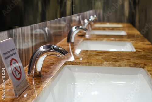 Closeup of a row of sinks with an elegant and exclusive feel with a sign saying please use the next available wash basin
