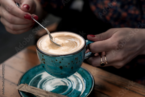 A young woman holds a coffee spoon and stirs hot coffee.
