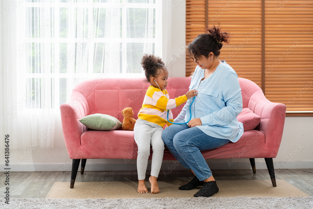 African American daughter playing with her mother in living room, girl role play as doctor with smile, parents spend quality time together with the kids relaxing enjoy weekend at home