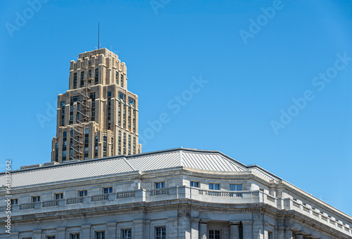 San Francisco, CA, USA - July 12, 2023: Beige tall UC Hastings tower peeks over top floor of white Federal Office building on United Nations Plaza under blue cloudscape photo