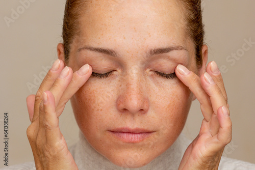 Middle aged caucasian woman of 40s with closed eyes holding fingers on eyelids to show eyes aging  photo