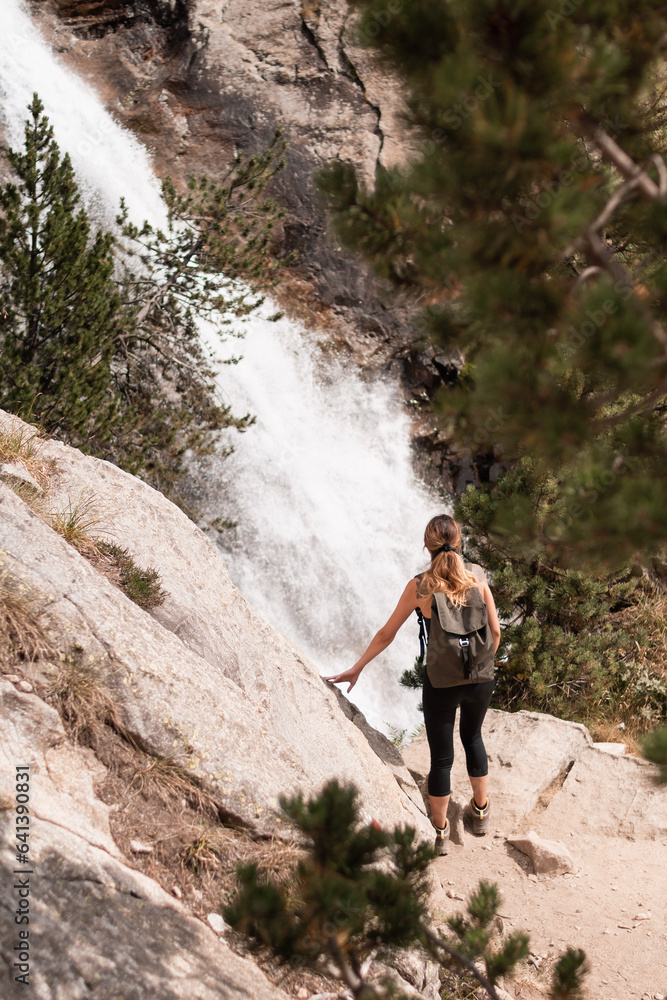 Young woman with backpack enjoying the Panticosa waterfalls in the Pyrenees during her trip through Huesca