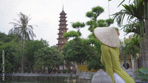 Portrait of Asian Vietnamese woman with Vietnam dress and straw hat in Tran Quoc temple pagoda. Tourist attraction landmark in urban city town of Hanoi, Vietnam. People lifestyle.