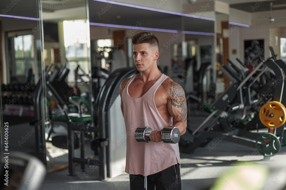 Handsome muscular athletic man with a tattoo on his arm does an exercise with dumbbells and pump his biceps in the sport gym Handsome muscular athletic man with a tattoo on his arm does an exercise with dumbbells and pump his biceps in the sport gym
