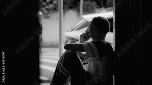 Thoughtful person from African American descent observing neighborhood from door front gazing with pensive contemplative expression, dramatic black and white