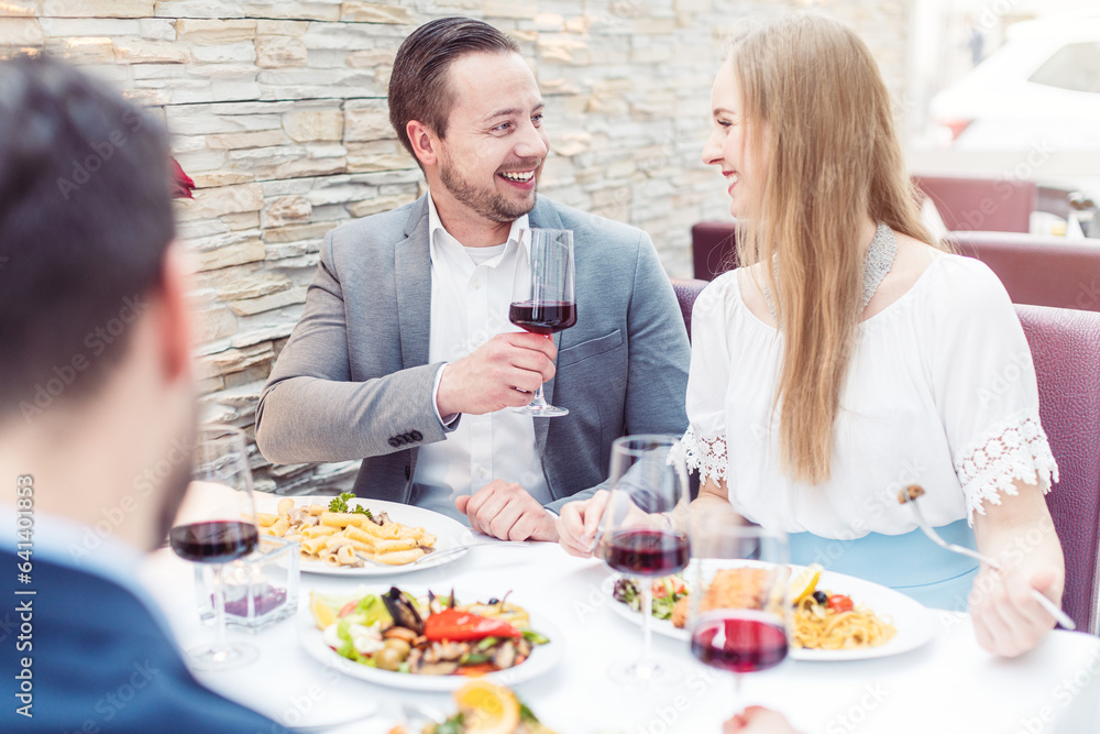 Four cheerful people enjoying drink and food in Italian restaurant