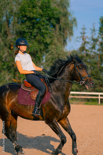 A horsewoman dressed in a helmet rides her beautiful black horse in a horse riding arena during a horseback ride