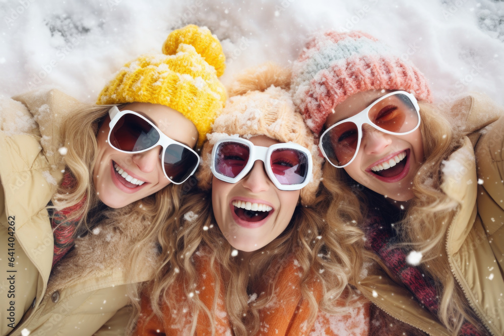 Fototapeta Three beautiful happy young women with sunglasses and winter clothing laying down in snow and having fun in ski resort Bukovel, winter holiday concept.