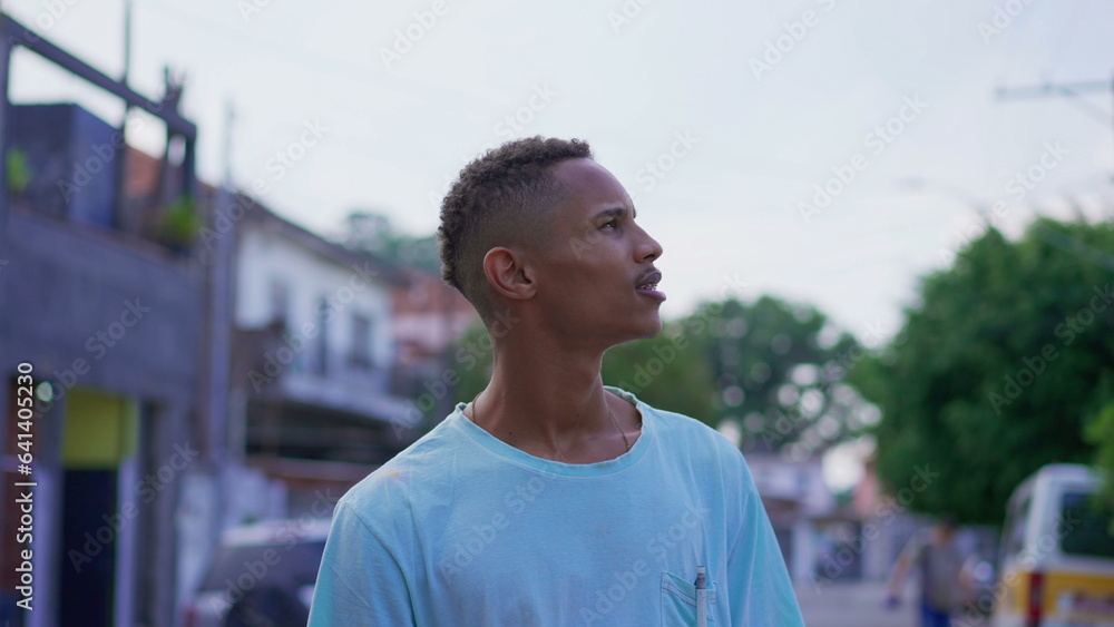 One pensive young black Brazilian man looking up at sky in contemplative and thoughtful expression. South American 20s person gazing at neighborhood One pensive young black Brazilian man looking up at sky in contemplative and thoughtful expression. South American 20s person gazing at neighborhood