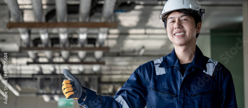 Portrait of Asian confident man construction worker in protective uniform suit and safety helmet showing thumbs up in unfinished building. Male engineer showing hand gesture sign at construction site photo